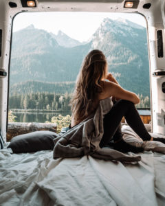 woman sitting in back of camper van looking at mountains